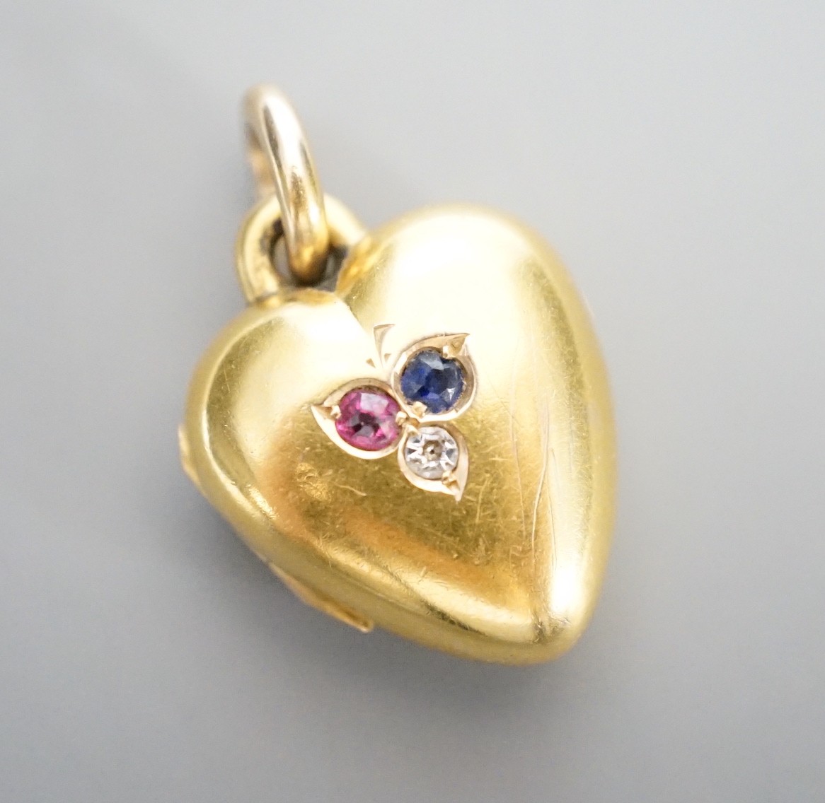 An Edwardian 15ct, sapphire, diamond and ruby set heart shaped locket, 17mm, gross weight 5.7 grams.